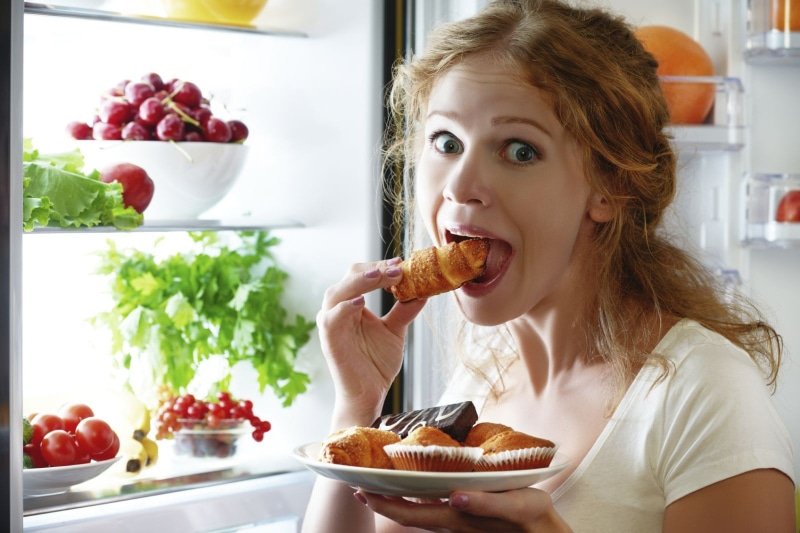 woman standing eating in front of fridge